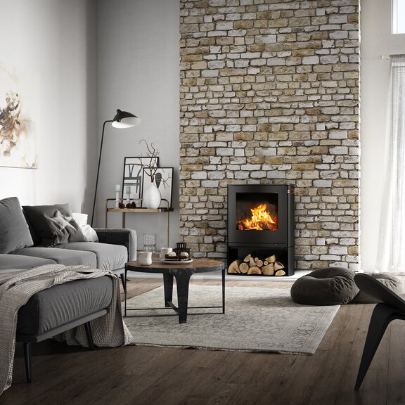Wood stove Q-TEE 2 C in black with wood compartment in its slightly oval shape as fireplaces in a rustic country house